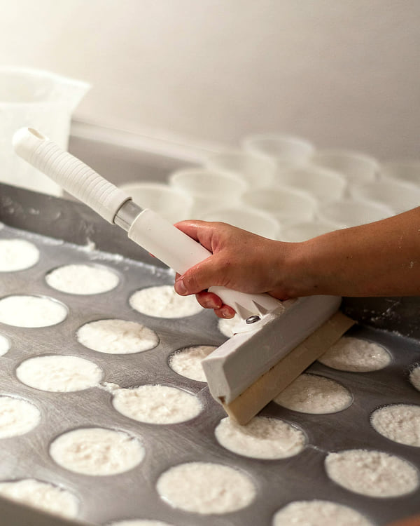 Une main remplit les moules à fromage posés en rangées sur une table de la fromagerie